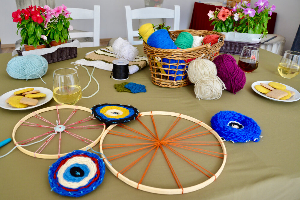 Table set with colorful yarn, weaving hoops and finished evil-eye woven pieces at the immersive weaving workshop in Athens