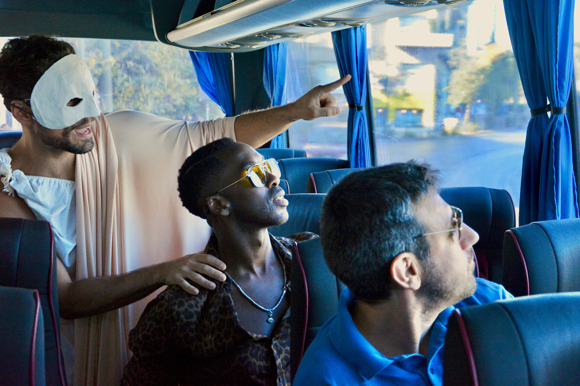 Masked actor in a toga performing for tourists aboard a bus during an interactive theatre experience in Athens