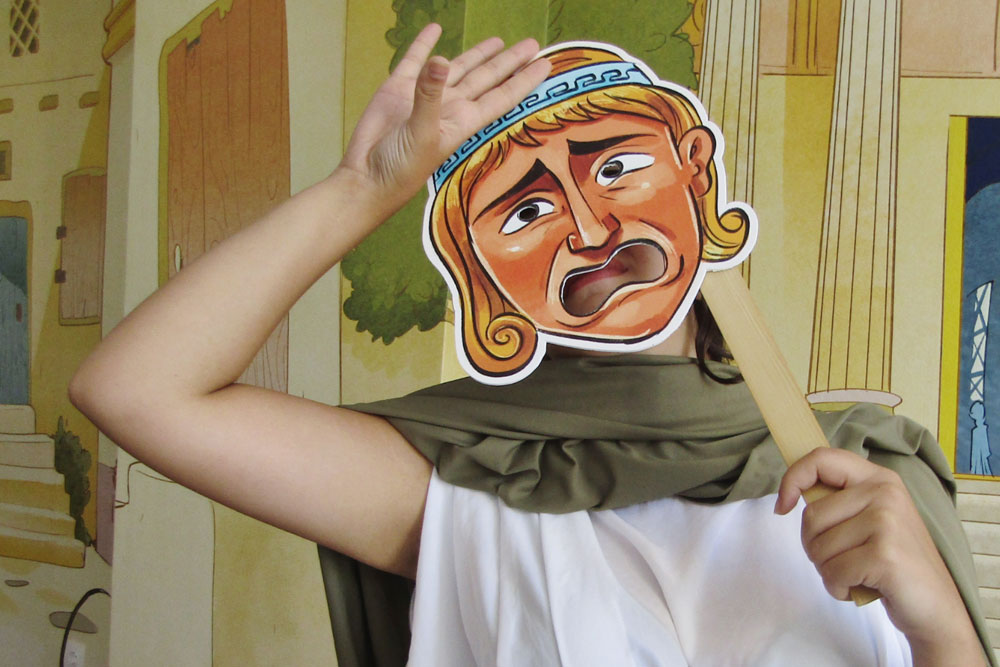 Guest in a toga holding a theatre mask at an interactive ancient Greece theatre experience in Athens