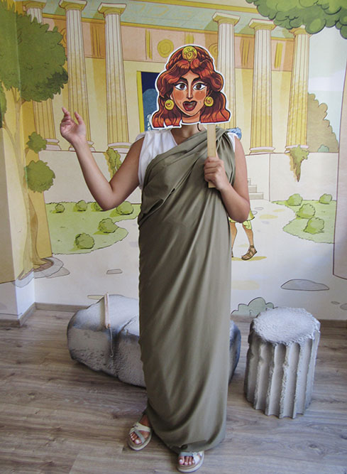 Participant dressed in a toga holding a theatre mask at an Athens Living Museum mythology experience